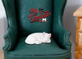 1:12 scale miniature white resin sleeping cat, curled up, shown on a green leather wing chair
