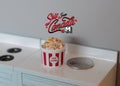 1:12 scale miniature popcorn in a red and white striped box, shown on a white kitchen counter beside a coin