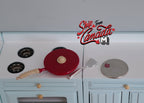 1:12 scale miniature red metal frying pan with lid and spatula, shown on a white stove beside a coin