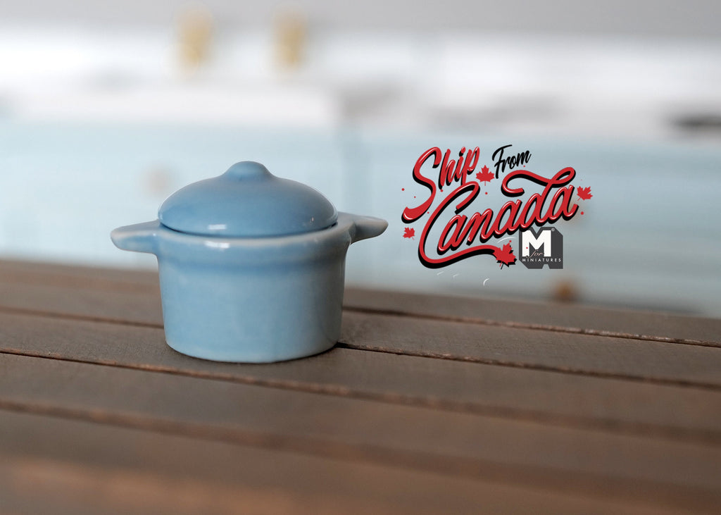 1:12 scale miniature light blue ceramic cooking pot with lid and 2 side handles, shown on a dark wood counter