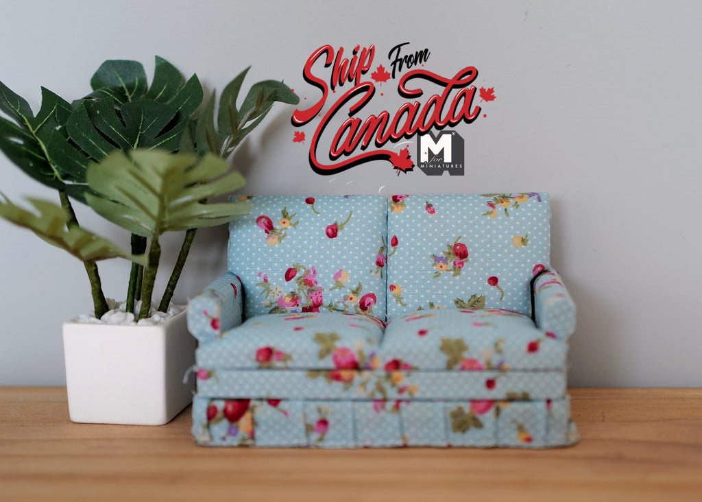 1:12 scale miniature upholstered loveseat in light blue floral print with pink roses, shown beside a potted plant