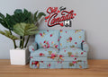1:12 scale miniature upholstered loveseat in light blue floral print with pink roses, shown beside a potted plant