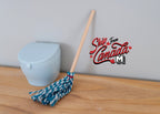 1:12 scale miniature kitchen mop with wood handle and blue and white string head, leaning on a wall by a toilet