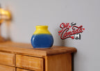 1:12 scale miniature ceramic plum vase with yellow and blue glaze, shown on a wood dresser