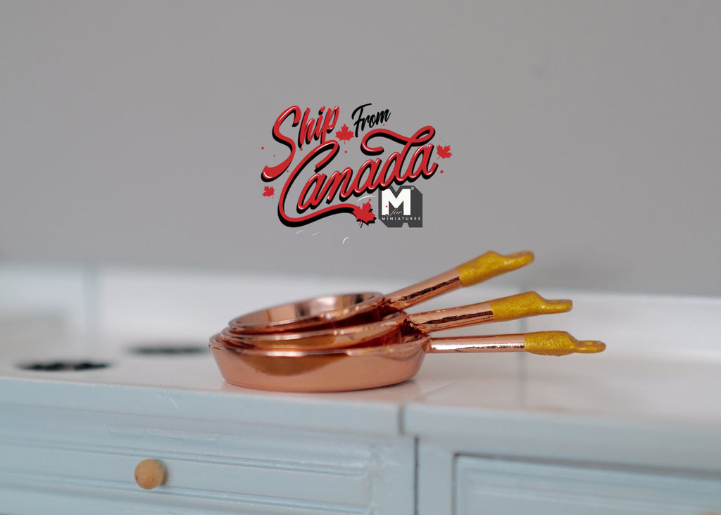 1:12 scale miniature metal frying pans in rose gold with gold handles, set of 3, nested on a kitchen counter