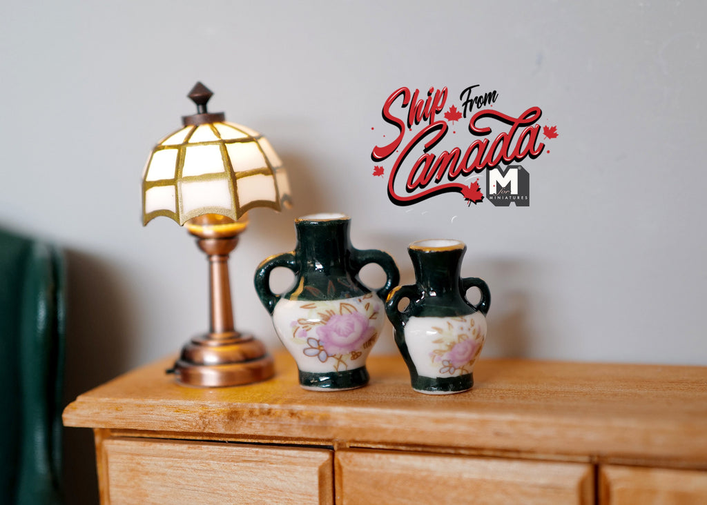 1:12 scale miniature dark green ceramic amphora vases with cream floral design, set of 2, shown on a dresser beside a lamp