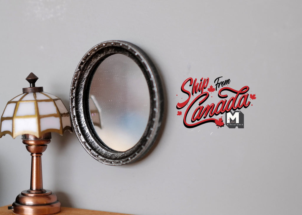 1:12 scale miniature ornate oval wall mirror in bronze, shown hanging on a gray wall beside a table lamp