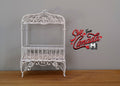 1:12 scale miniature metal baby crib in white with scroll canopy and wire sides, shown on a wood floor