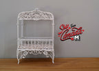 1:12 scale miniature metal baby crib in white with scroll canopy and wire sides, shown on a wood floor