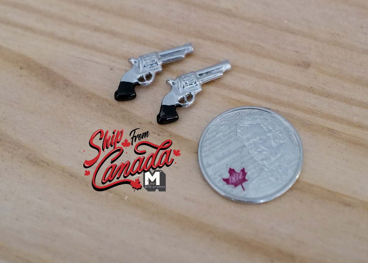 1:12 scale miniature pistol props in silver with black grips, set of 2, on a wood surface beside a coin for scale