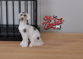 1:12 scale miniature sitting dog figurine with white and black spotted coat, shown on a wood floor by a pet crate