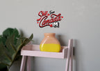 1:12 scale miniature ceramic two tone flower pot in peach and yellow, jug shape, shown on a pink shelf beside a plant
