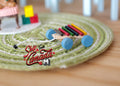 1:12 scale miniature primitive pull toy xylophone with rainbow bars and blue wheels, shown on a green braided rug