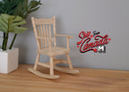 1:12 scale miniature unpainted wood rocking chair with spindle back and arms, on a wood floor beside a potted plant
