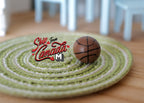 1:12 scale miniature basketball in brown with black lines, shown on a green round woven rug