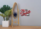 1:12 scale miniature metal cheval mirror in brass, oval and free standing, shown beside a potted plant