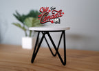 1:12 scale miniature wood and metal round side table in white with black crossed hairpin legs, beside a plant