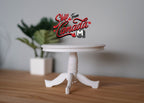 1:12 scale miniature white wood round pedestal dining table with 3 feet, shown on a wood floor beside a plant