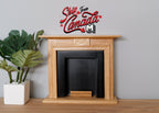1:12 scale miniature honey wood fireplace with black firebox and hearth, shown beside a potted plant