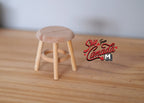 1:12 scale miniature unpainted wood round stool with 3 legs and stretcher rungs, shown on a wood surface