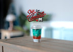 1:6 scale miniature iced summer drink cup with clear lid, layered red and teal drink, shown on a wood table