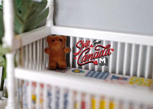 1:12 scale miniature bear cub doll in brown with flocked skin, shown sitting in a white crib