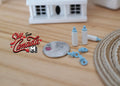 1:12 scale miniature baby feeding set in blue with bottles and pacifiers, shown beside a coin for scale