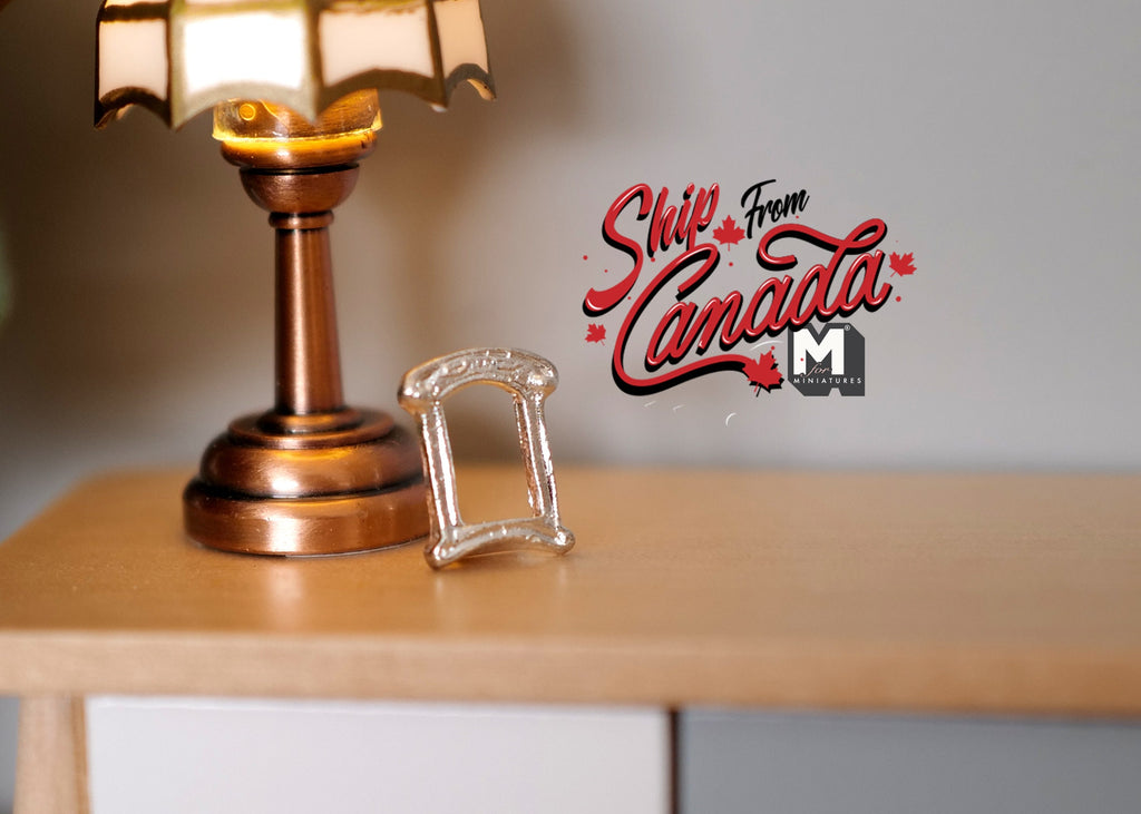 1:12 scale miniature small rectangular metal photo frame in silver with arched top, on a wood dresser beside a lamp