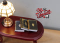 1:12 scale miniature hardcover books in dark green and black with gold cover designs, set of 3, on a table by a lamp