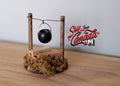 1:12 scale miniature wood fire pit with log pile and hanging black pot on a post frame, shown on a wood surface