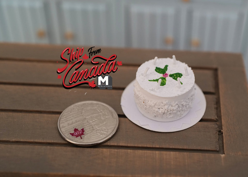 1:12 scale miniature white round birthday cake with candles and green leaf decoration, on a plate beside a coin