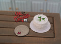 1:12 scale miniature white round birthday cake with candles and green leaf decoration, on a plate beside a coin
