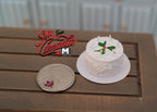1:12 scale miniature white round birthday cake with candles and green leaf decoration, on a plate beside a coin