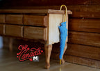 1:12 scale miniature closed umbrella in blue with gold style hook handle, shown hanging on a wood side table