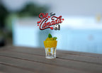 1:12 scale miniature glass of lime soda with ice and lemon slice, yellow drink with green garnish, shown on a wood table
