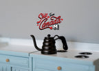1:12 scale miniature metal gooseneck coffee drip kettle in black with lid, shown on a white stove with blue cabinets