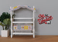 1:12 scale miniature baby crib in white with fabric canopy and printed mattress, shown beside a potted plant