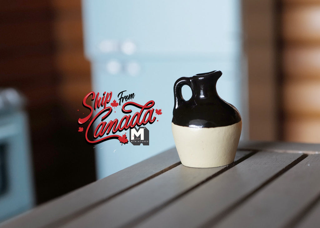 1:12 scale miniature ceramic crock jug with handle in black and cream glaze, shown on a gray wood table