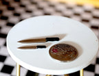 1:12 scale miniature kitchen knives with black handles, set of 2, shown on a round white table beside a coin