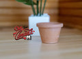1:12 scale miniature clay flower pot in terracotta with a tapered shape and rim, shown on a wood floor