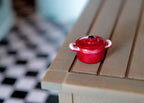 1:12 scale miniature metal cooking pot with lid in red with two handles, shown on a wood table