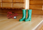 1:12 scale miniature rubber rain boots in green, one pair, tall wellington style, shown on a wood floor by a dresser