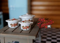 1:12 scale miniature ceramic cooking pots with lids in white with floral pattern, set of 3, on a wood table