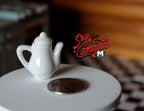 1:12 scale miniature white porcelain water pot with tall neck, handle and lid, shown on a round table beside a coin