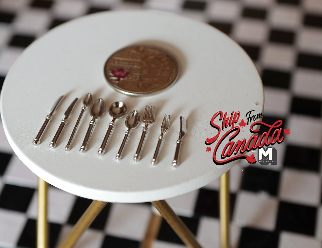 1:12 scale miniature metal flatware set in silver, knives, forks and spoons, set of 9, on a white table with a coin