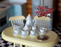 1:12 scale miniature plain white porcelain tea set of 15 with teapot, cups, saucers and plates, on a yellow table