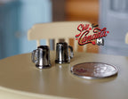 1:12 scale miniature metal beer mugs in pewter with handles, set of 2, shown on a round table beside a coin
