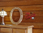 1:12 scale miniature metal oval picture frame in gold with embossed flowers and fruits, shown on a wood dresser