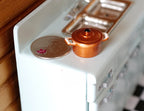 1:12 scale miniature metal cooking pot with lid in copper orange with two handles, shown beside a coin for scale
