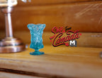 1:12 scale miniature aqua blue pedestal vase with textured translucent body, shown on a wood shelf